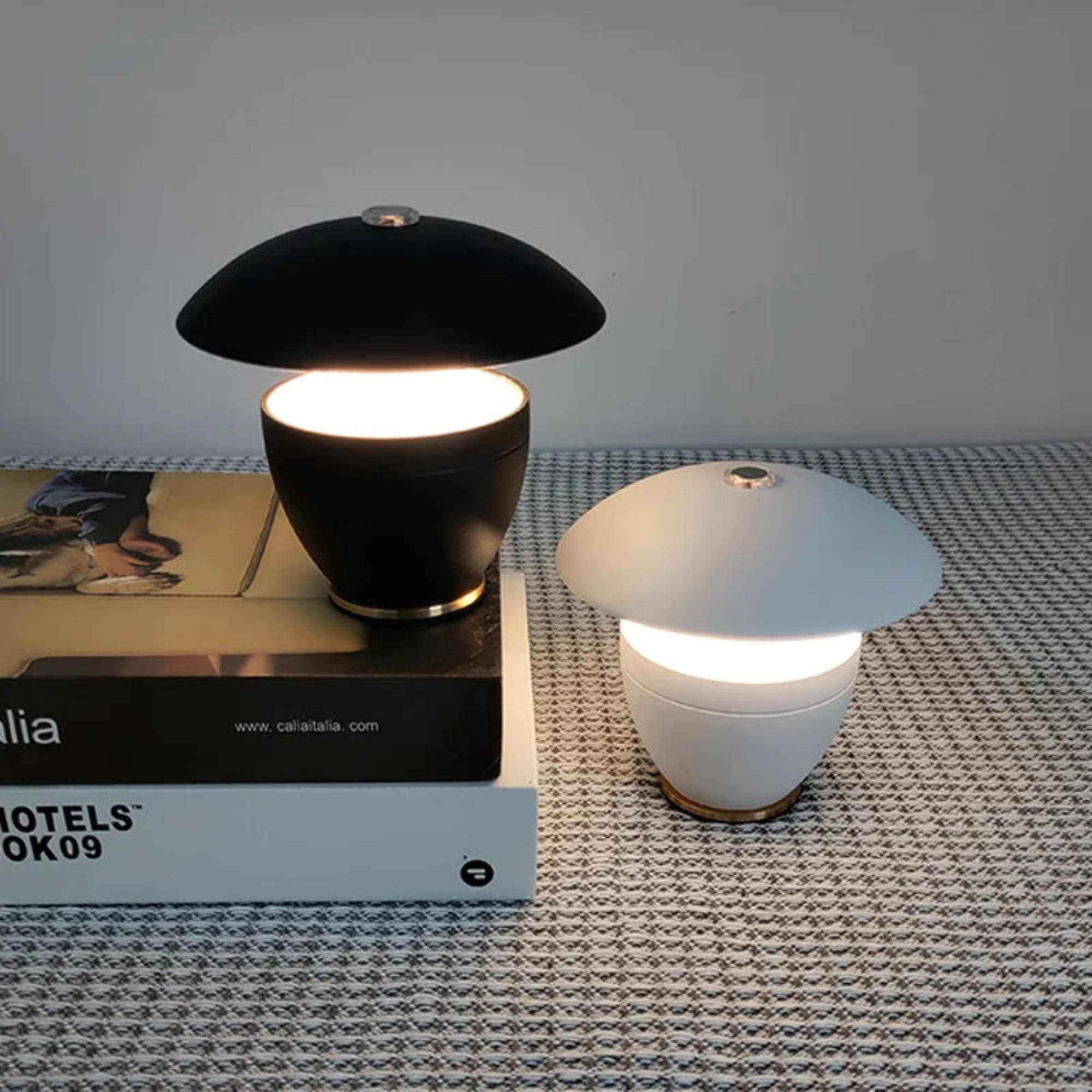 Two table lamps, one black and one white, on a textured surface with a magazine underneath.