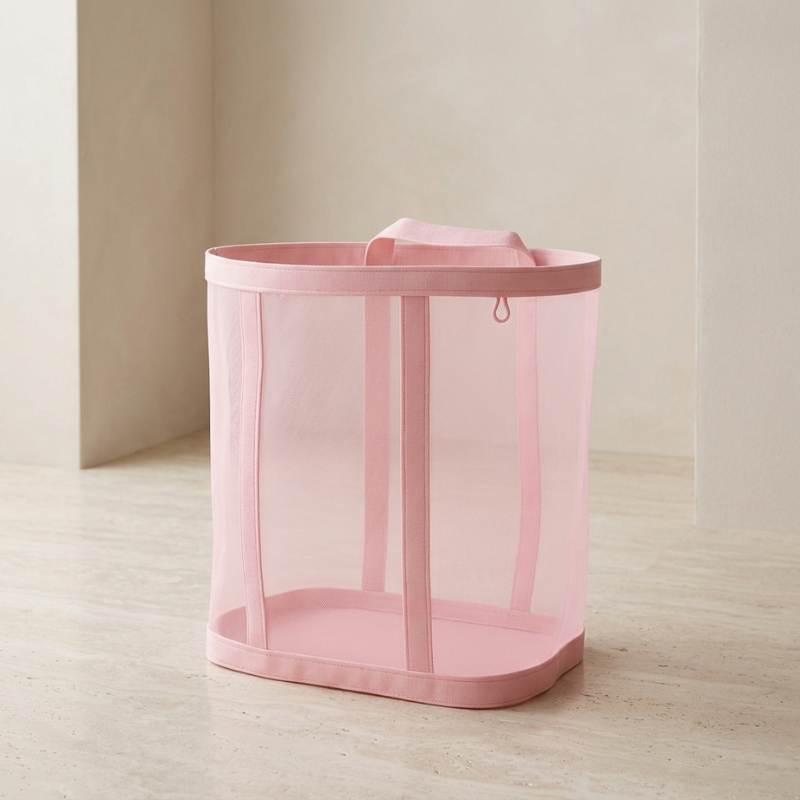 Pink mesh laundry basket on a light wooden floor with a neutral wall background