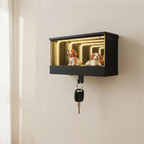 A black wall-mounted key safe display box with warm LED lighting inside, holding two small dog figurines, with a key hanging from the front hook, shown mounted on a beige wall.