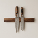 Two knives with wooden handles on a magnetic strip against a light background