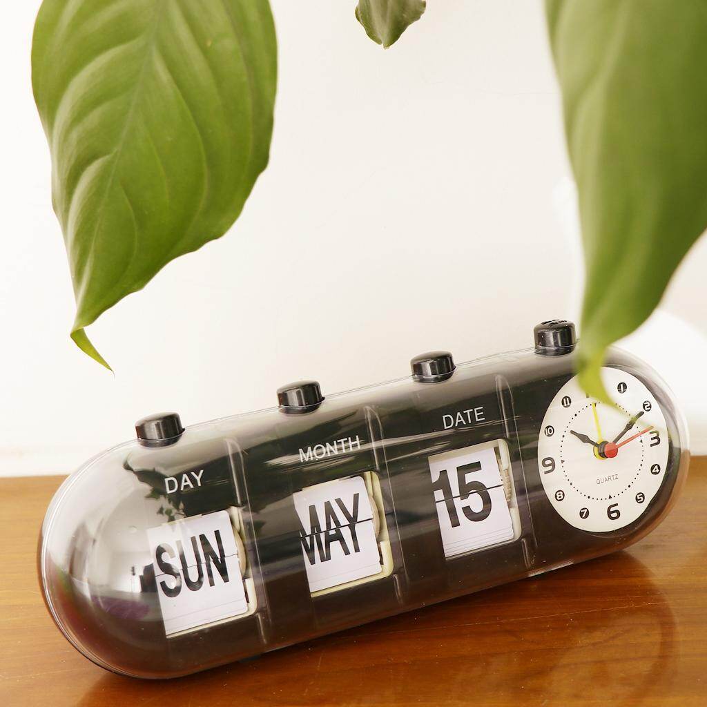 Tabletop clock with calendar display on a wooden surface with green leaves in the background