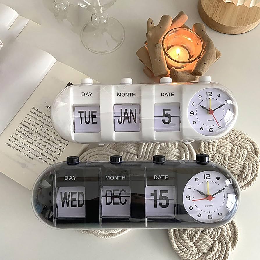 Dual clock with calendar display on a surface with a candle and book in the background