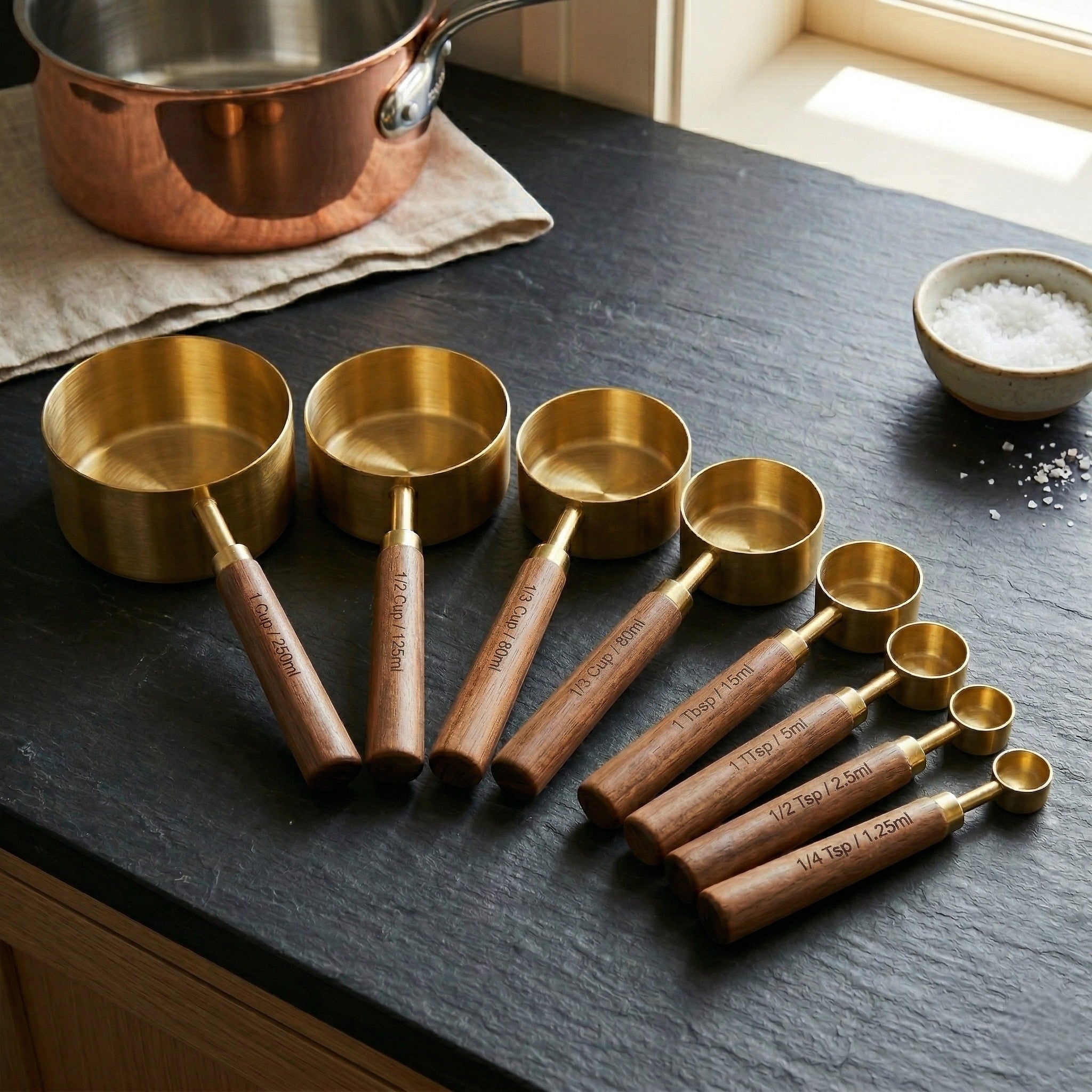 Set of brass measuring cups with wooden handles on a dark surface