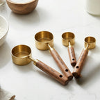 Set of brass measuring cups with wooden handles on a marble surface