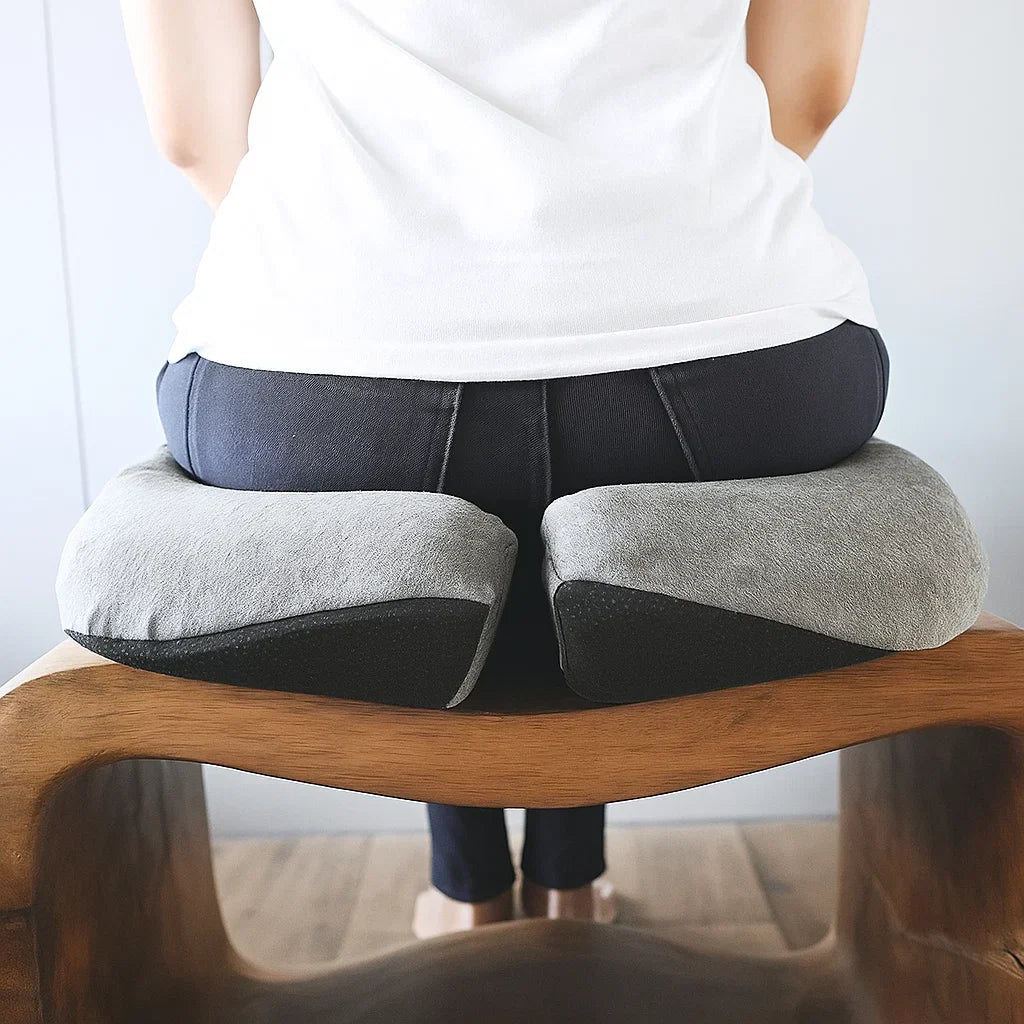 Person sitting on a wooden stool with a gray cushion on their back