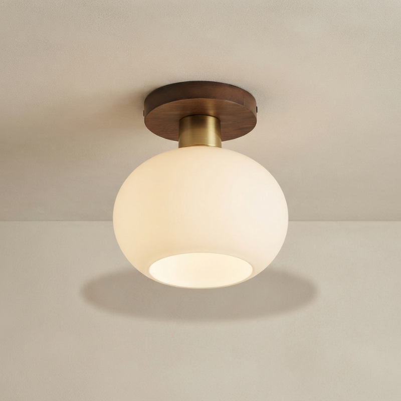A modern semi-flush mount ceiling light fixture with a frosted white spherical glass shade, a brass-finished neck, and a dark brown circular ceiling canopy, shown installed on a textured off-white ceiling.