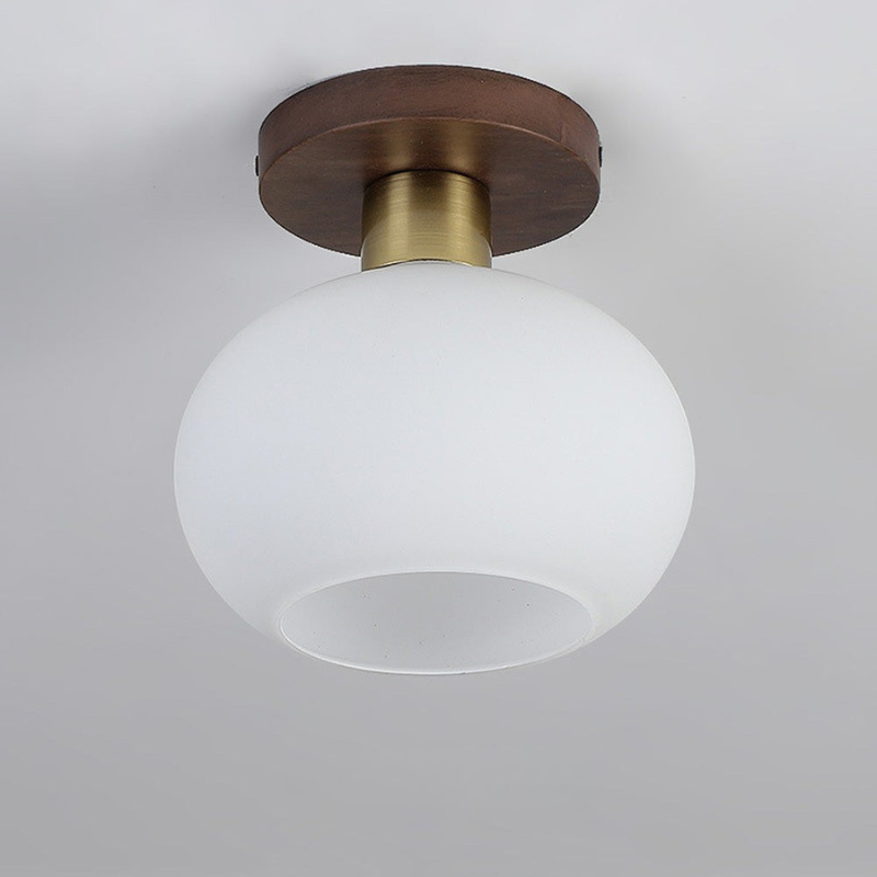 A modern semi-flush mount ceiling light fixture featuring a large frosted white glass globe shade, a brushed brass cylindrical neck, and a round dark brown wood ceiling canopy, shown against a neutral light gray ceiling.
