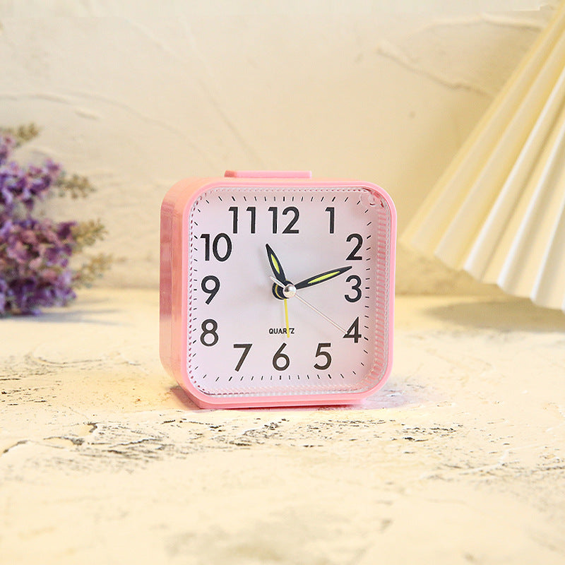 Pink alarm clock on a light wooden surface with a blurred background