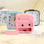 Pink toy camera with a small lens and flash on a wooden surface with clocks in the background.
