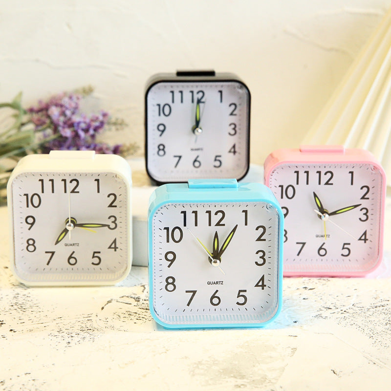 Four small alarm clocks in different colors on a light surface with a blurred background