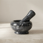 A dark polished stone mortar and pestle set on a light beige surface against a neutral beige background.