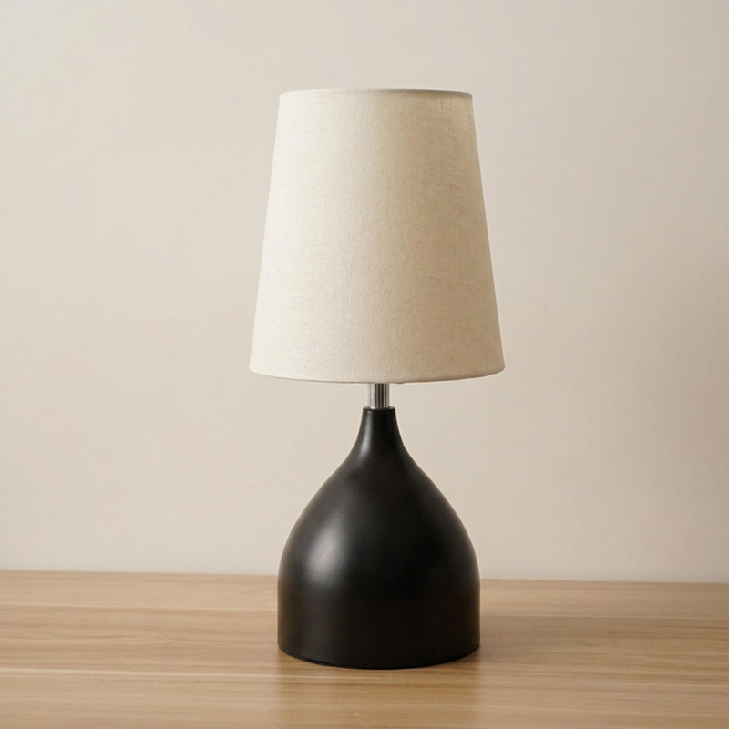 Table lamp with a black base and beige shade on a wooden surface.