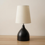 Table lamp with a black base and beige shade on a wooden surface.