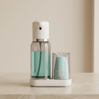 Clear spray bottle with green liquid and a stack of cups on a beige surface