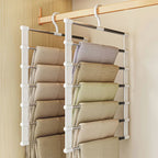 Hanging multi-layered organizer with folded clothes on a wooden rod against a beige wall.