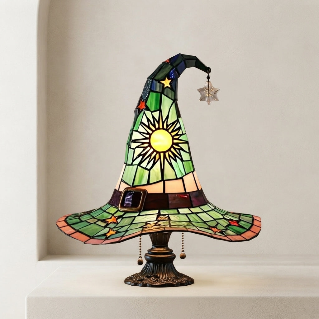 A stained-glass-style witch hat table lamp with a green and yellow sun design, displayed on a pedestal against a neutral beige background.