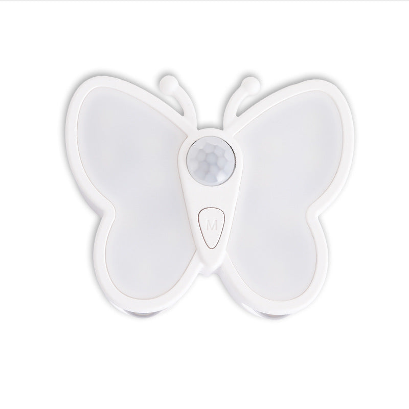 A white butterfly-shaped motion sensor night light with a central circular sensor and a small button marked with an 'M', shown on a plain white background.