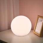 Spherical white lamp on a surface with a pink wall and framed picture in the background