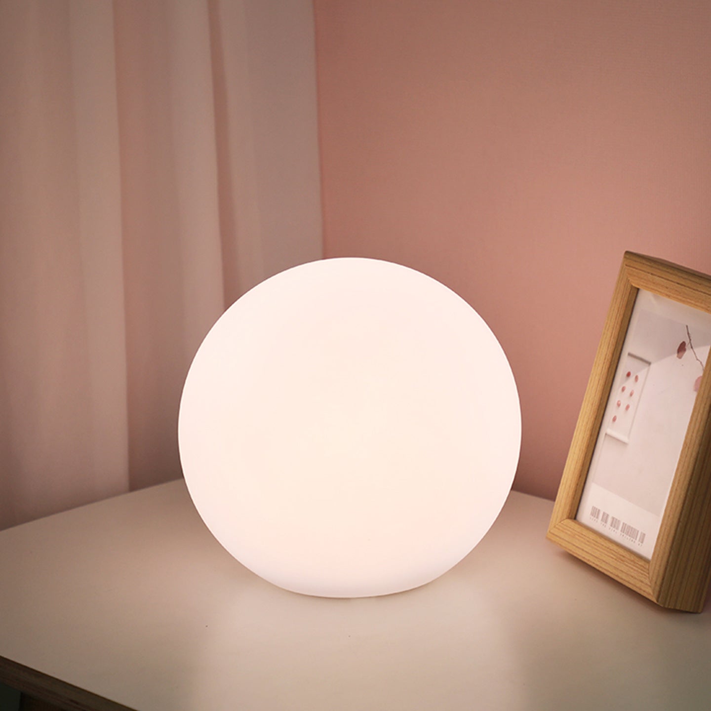 Spherical white lamp on a surface with a pink wall and framed picture in the background