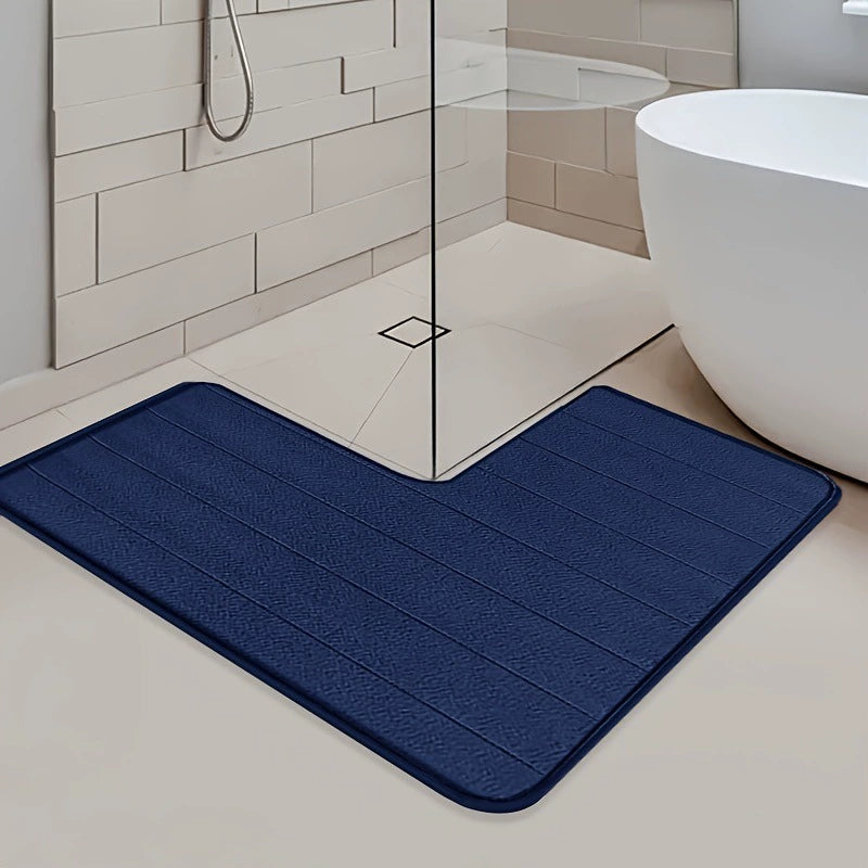Navy blue bath mat on a bathroom floor with a shower and bathtub in the background.
