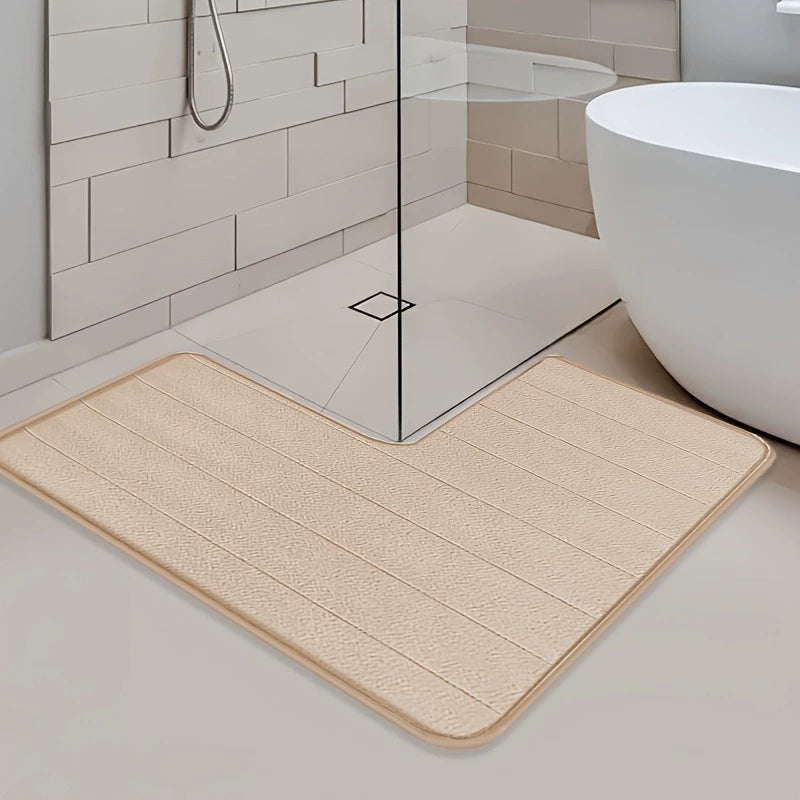 Beige bath mat on a bathroom floor with a shower and bathtub in the background.