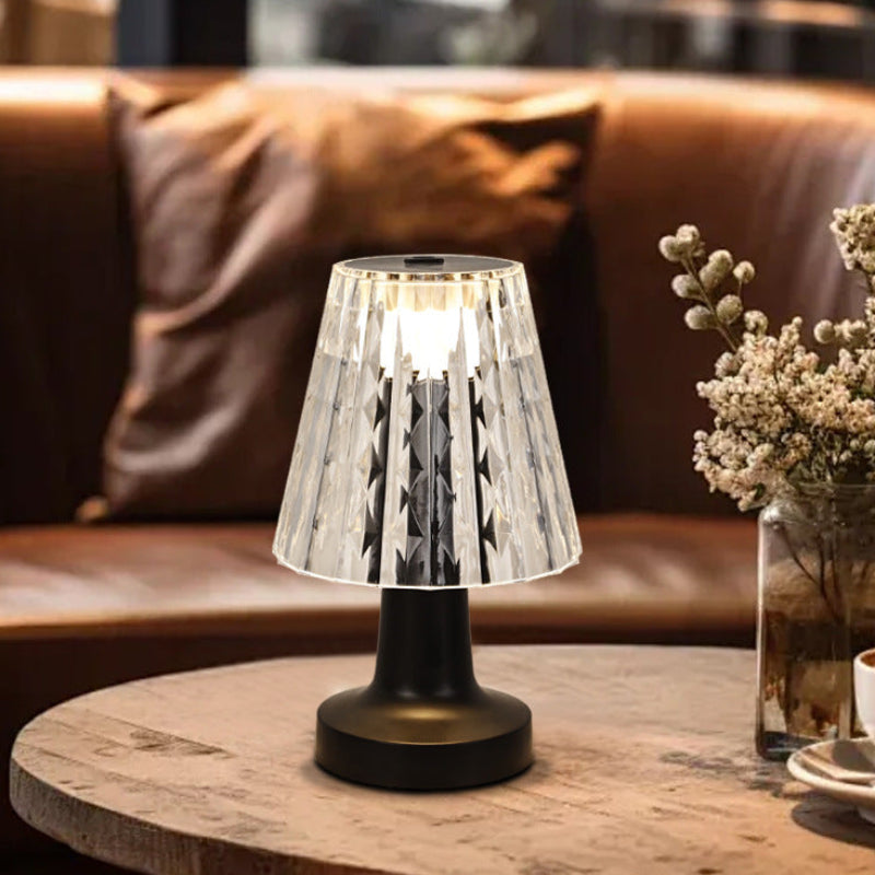 Table lamp on a wooden table with a cup of coffee and decorative plants in the background.