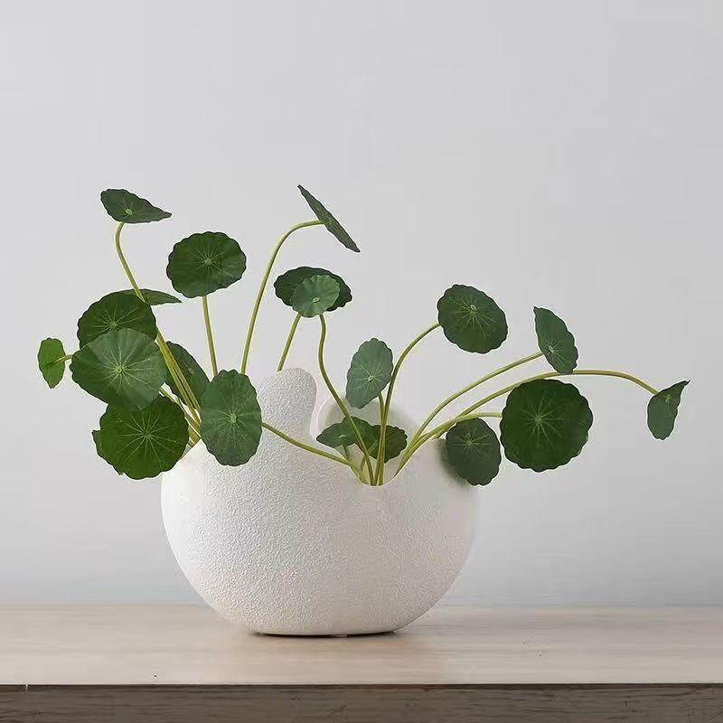 White textured vase with green leaves on a light wooden surface and gray background