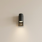 A modern black cylindrical outdoor wall sconce with a built-in motion sensor, mounted on a plain beige wall and casting a warm light downward.