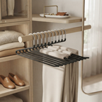 A black metal hanger organizer with multiple hangers and a flat lower rack, shown hanging in a light wood closet organizer with folded beige garments and neutral decor.
