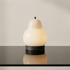 A sculptural table lamp with a pear-shaped frosted glass shade in warm off-white, resting on a dark circular base with a dark leather band, set against a neutral beige background.