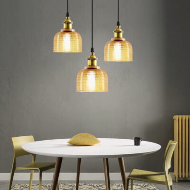 Three gold pendant lights hanging above a round white table with green chairs against a gray wall.