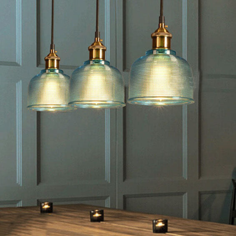 Three pendant lights with glass shades and gold fixtures hanging above a wooden surface.