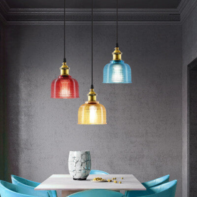 Three colorful pendant lights hanging above a dining table with chairs.