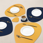 Set of yellow and blue placemats with white plates, silver forks, and a cup on a beige surface.