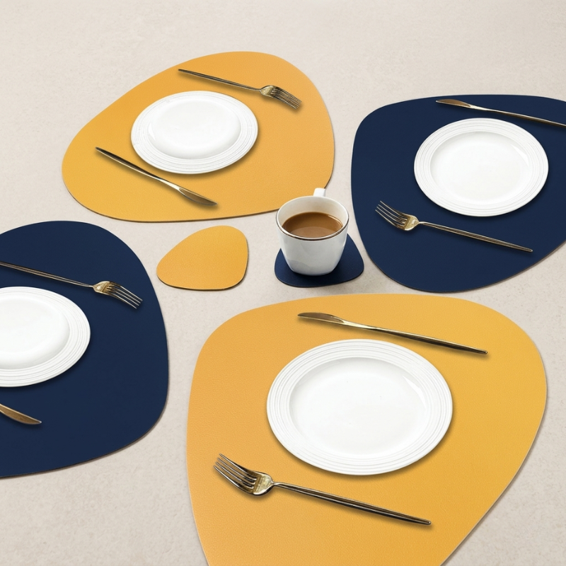 Set of yellow and blue placemats with white plates, silver forks, and a cup on a beige surface.