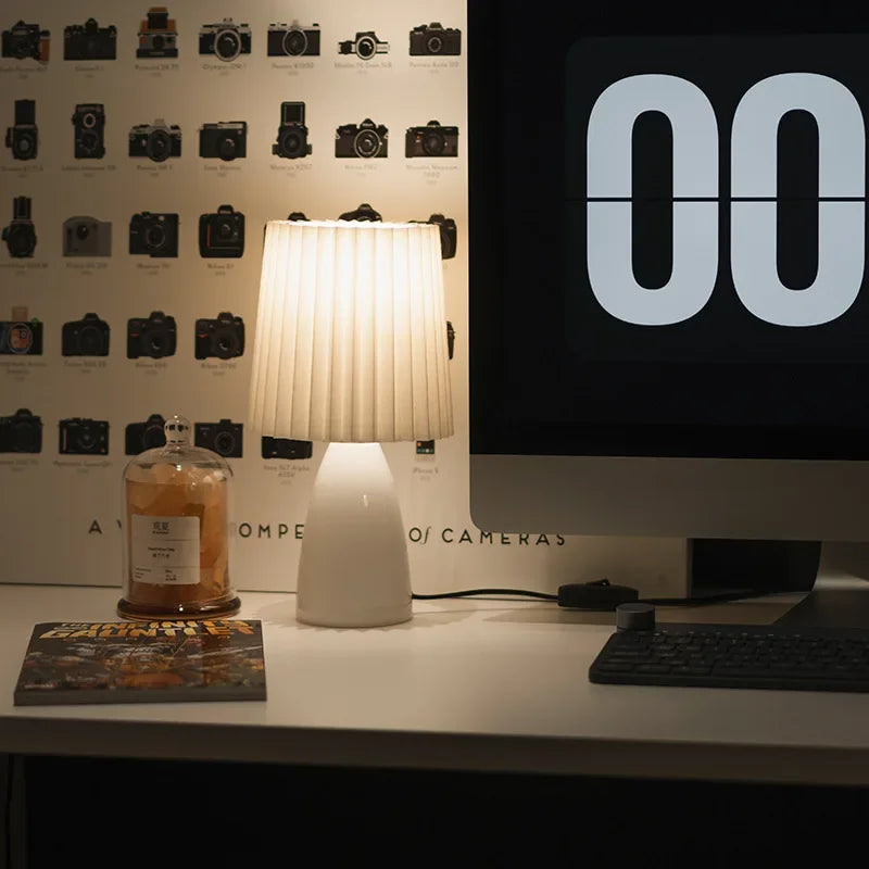 Desk setup with a lamp, computer monitor displaying '00', and a bottle on a wall with camera designs.