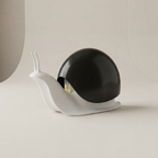 A modern snail-shaped lamp with a glossy black shell and a matte white body, shown on a minimalist beige background.