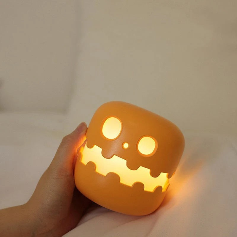 A hand holds a small orange pumpkin-shaped night light with a glowing jack-o'-lantern face. The light is turned on and casting a warm yellow glow, with white 'Z' sleep marks floating near it against a soft beige background.