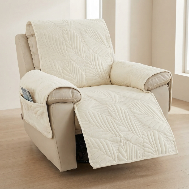 A cream-colored quilted recliner cover with a leaf pattern draped over a beige recliner chair in a bright room with light wood floors.