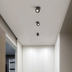 Three black ceiling spotlights installed in a modern white hallway ceiling.