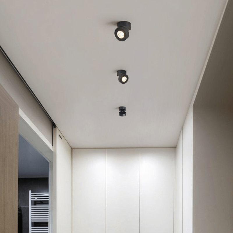 Three black ceiling spotlights installed in a modern white hallway ceiling.