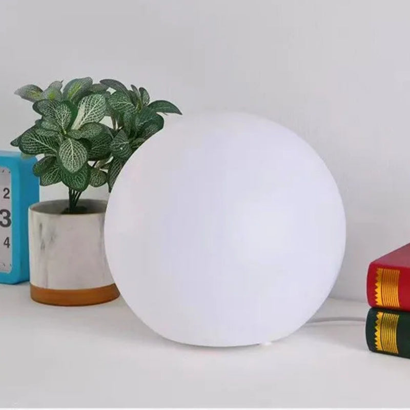 White spherical lamp on a table with books and a plant