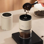 Coffee grinder with coffee beans being added on a light surface