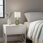 White nightstand with a green clock and lamp next to a bed in a bedroom.
