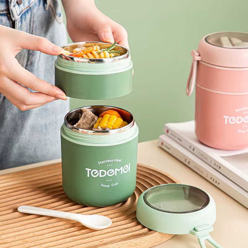 Green soup cup with food, wooden spoon, and pink container on a wooden surface.