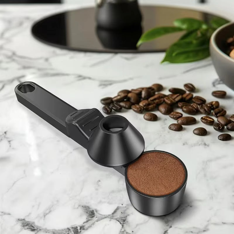 Black coffee scoop with ground coffee on a marble surface with coffee beans and a teapot in the background.