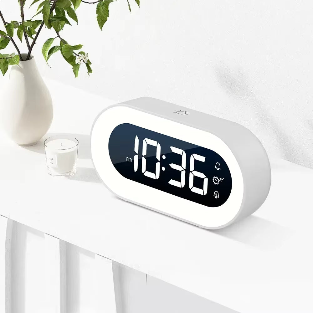 Digital clock on a white surface with a plant and candle in the background