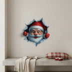 A 3D Santa Claus wall decal showing Santa peeking through a torn hole in a beige wall above a bench with a throw blanket and a plaid pillow.