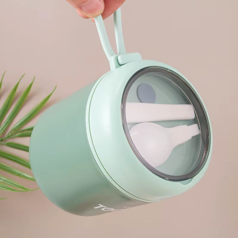 Mint green travel mug with spoon and fork inside, held by a hand against a beige background.
