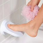 Person using a pink loofah on their foot next to a white stool in a tiled bathroom.